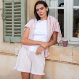 Woman in a white outfit with a pink cardigan standing in front of a window.