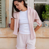 Woman wearing a light pink cardigan, white top, and shorts standing on a porch.