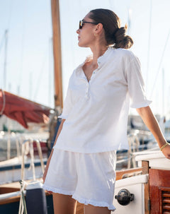 Woman in a white outfit standing on a boat with a scenic background