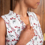 Woman wearing a white sleeveless top with red floral pattern, holding her collar.