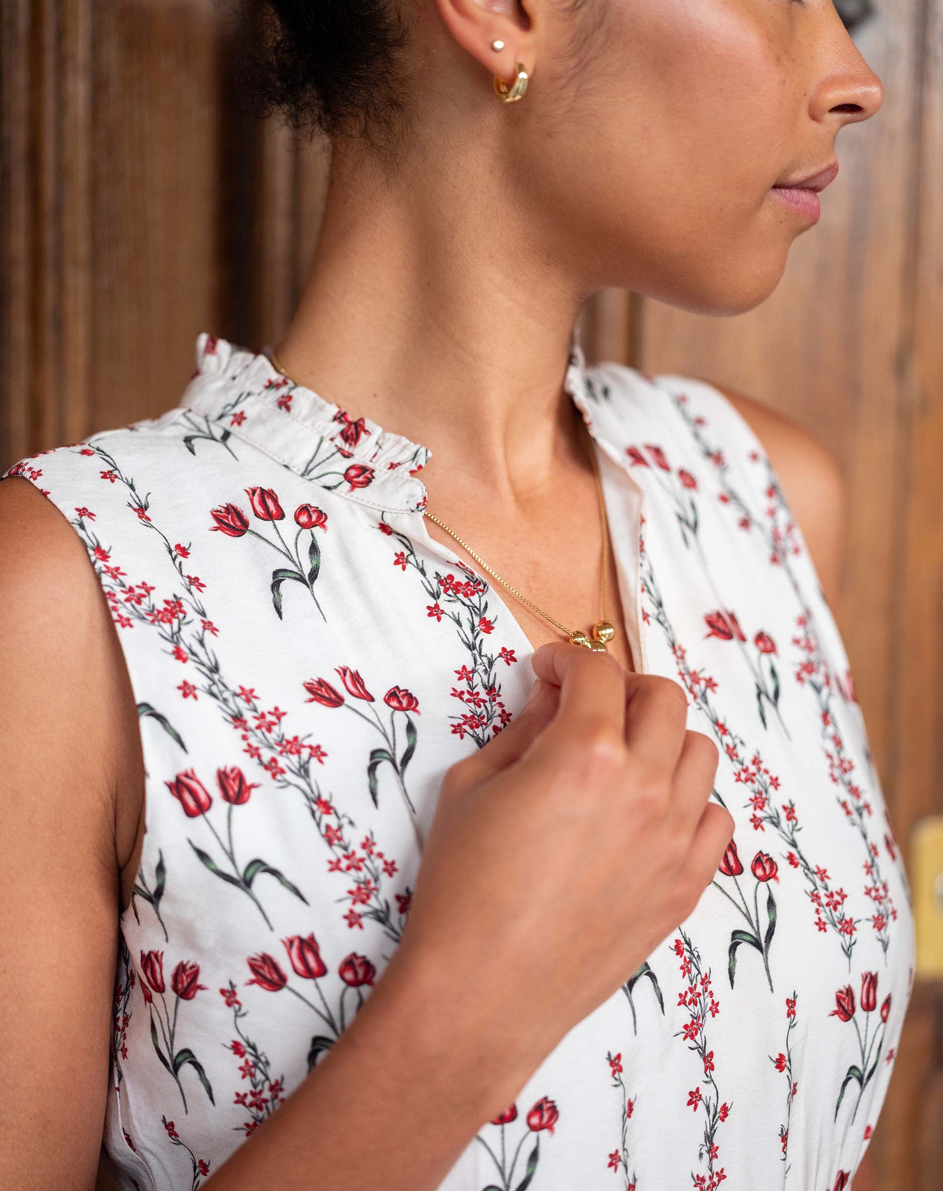 Woman wearing a white sleeveless top with red floral pattern, holding her collar.