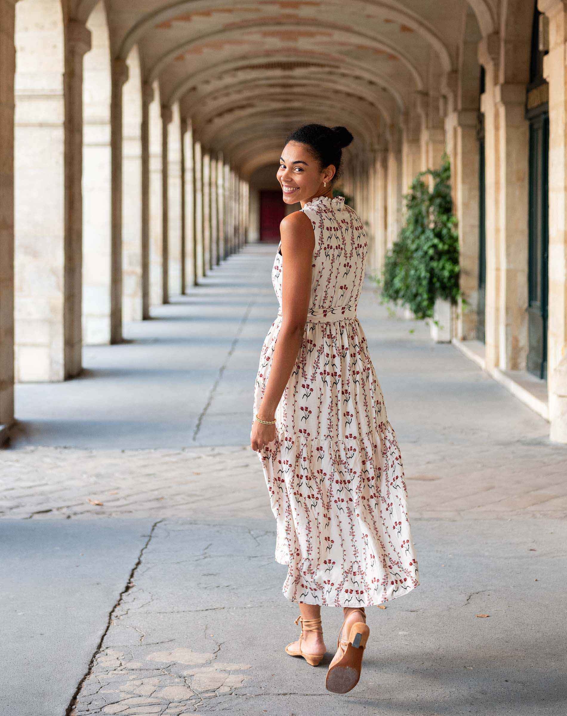 Woman in a floral dress walking through an architectural corridor.