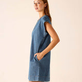 Woman wearing a blue denim dress against a beige background