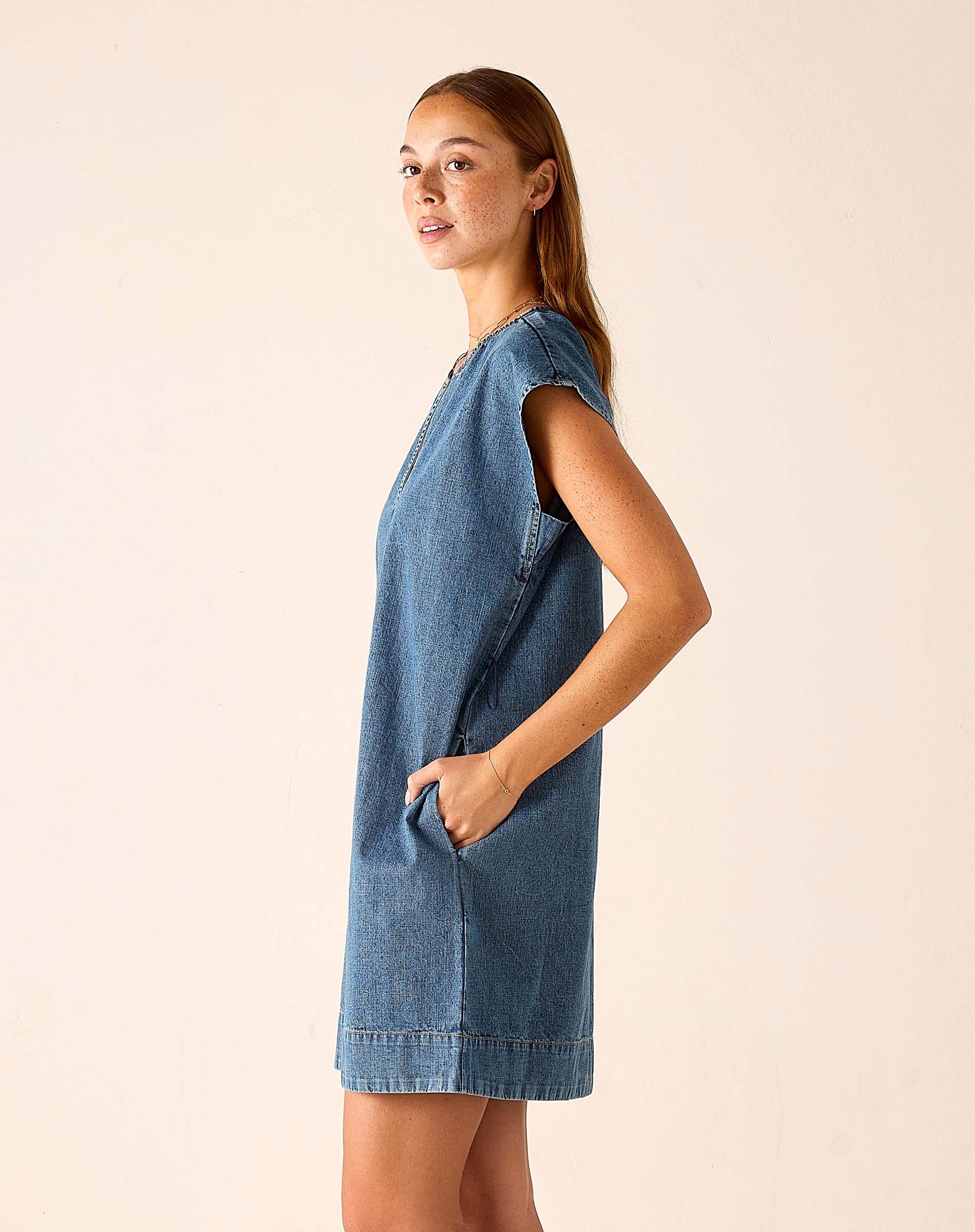 Woman wearing a blue denim dress against a beige background