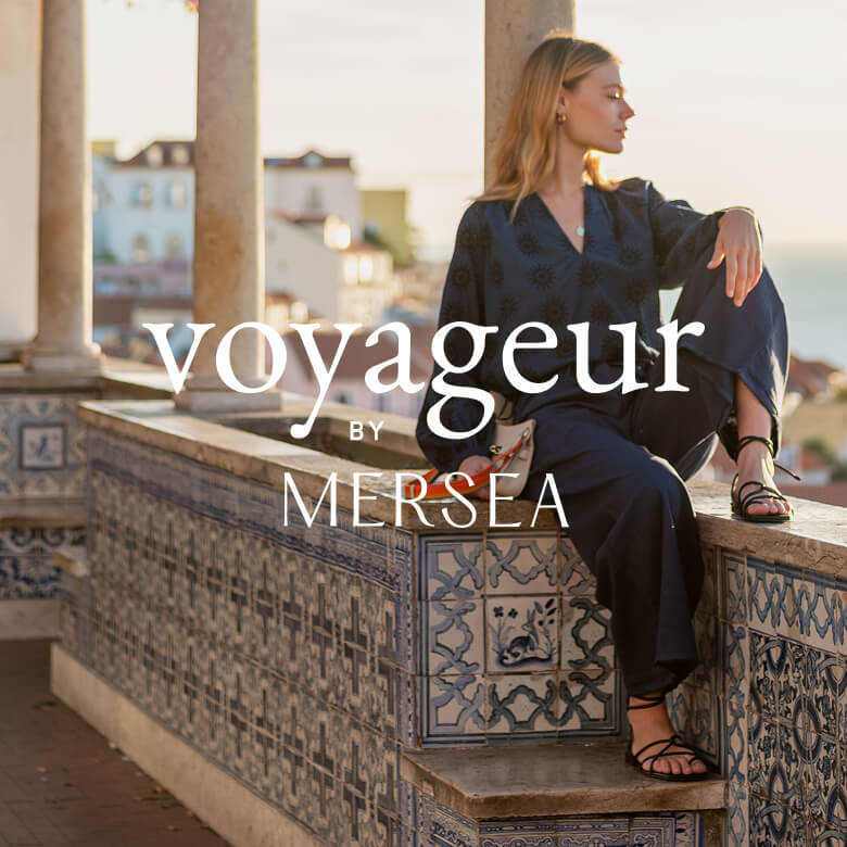 logo overlay photo: Voyageur by MERSEA - image of women sitting on a ledge in a linen navy set overlooking Lisbon, Portugal 