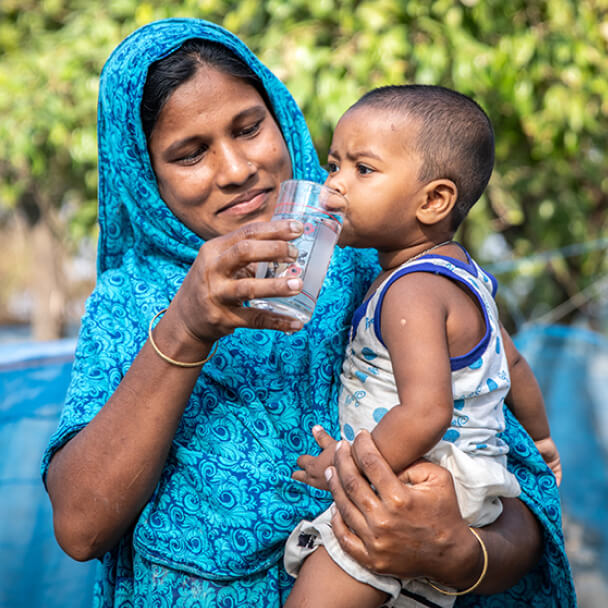 Woman Holding Baby and Feeding him Water out of the Glass