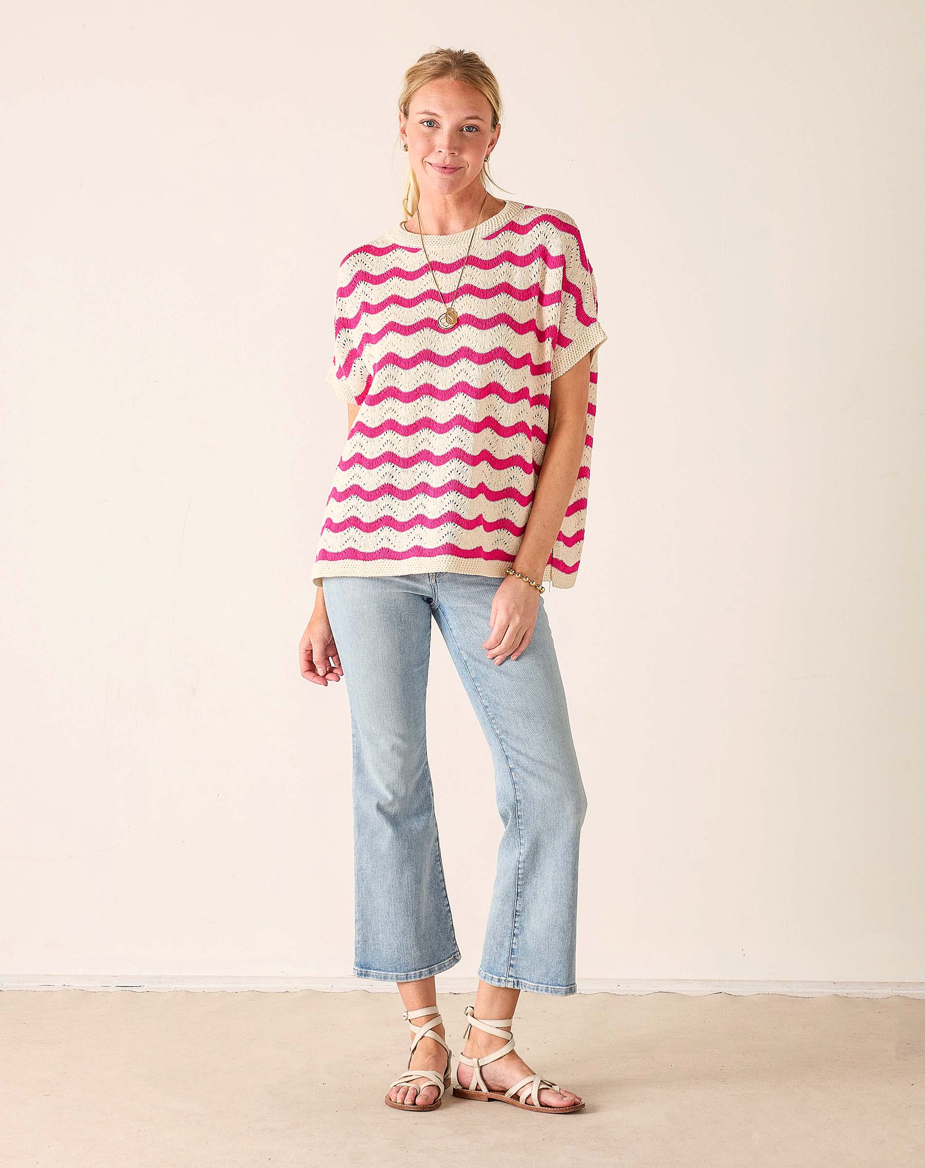 Woman wearing a pink and white striped shirt with light blue jeans on a plain background