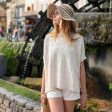 Woman in a white lace top and shorts standing in front of an anchor sculpture.