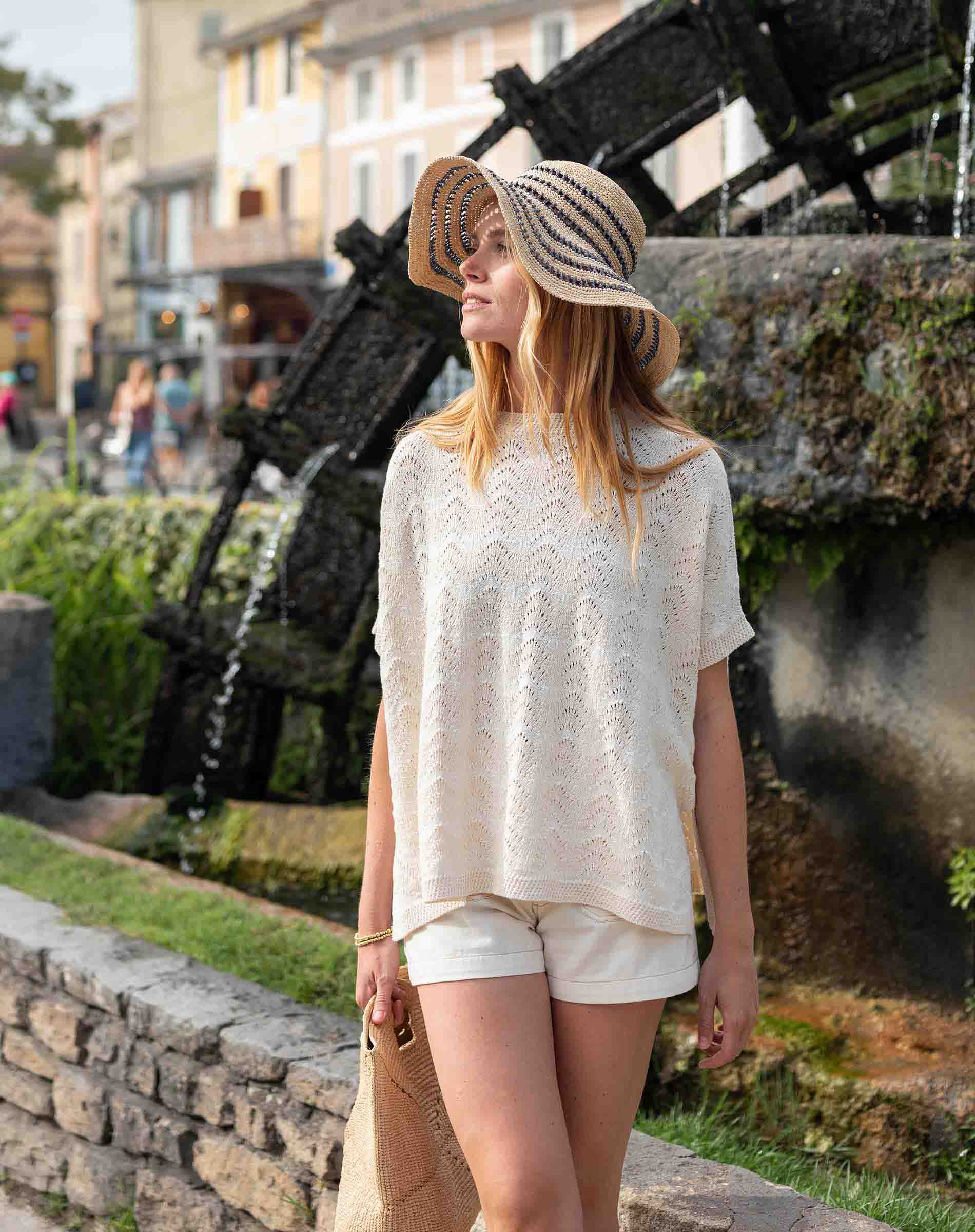 Woman in a white lace top and shorts standing in front of an anchor sculpture.