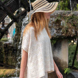 Woman wearing a wide-brimmed hat and white outfit by a water fountain