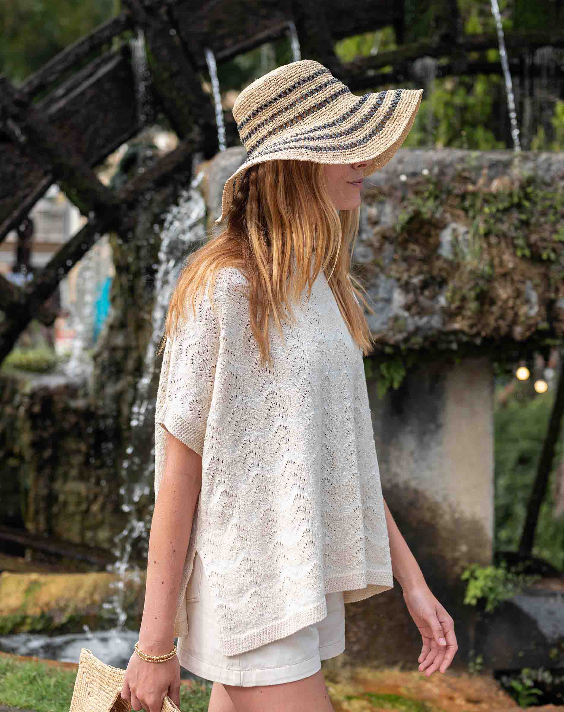 Woman wearing a wide-brimmed hat and white outfit by a water fountain