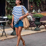 Woman walking outdoors wearing a blue and white striped shirt and denim shorts.