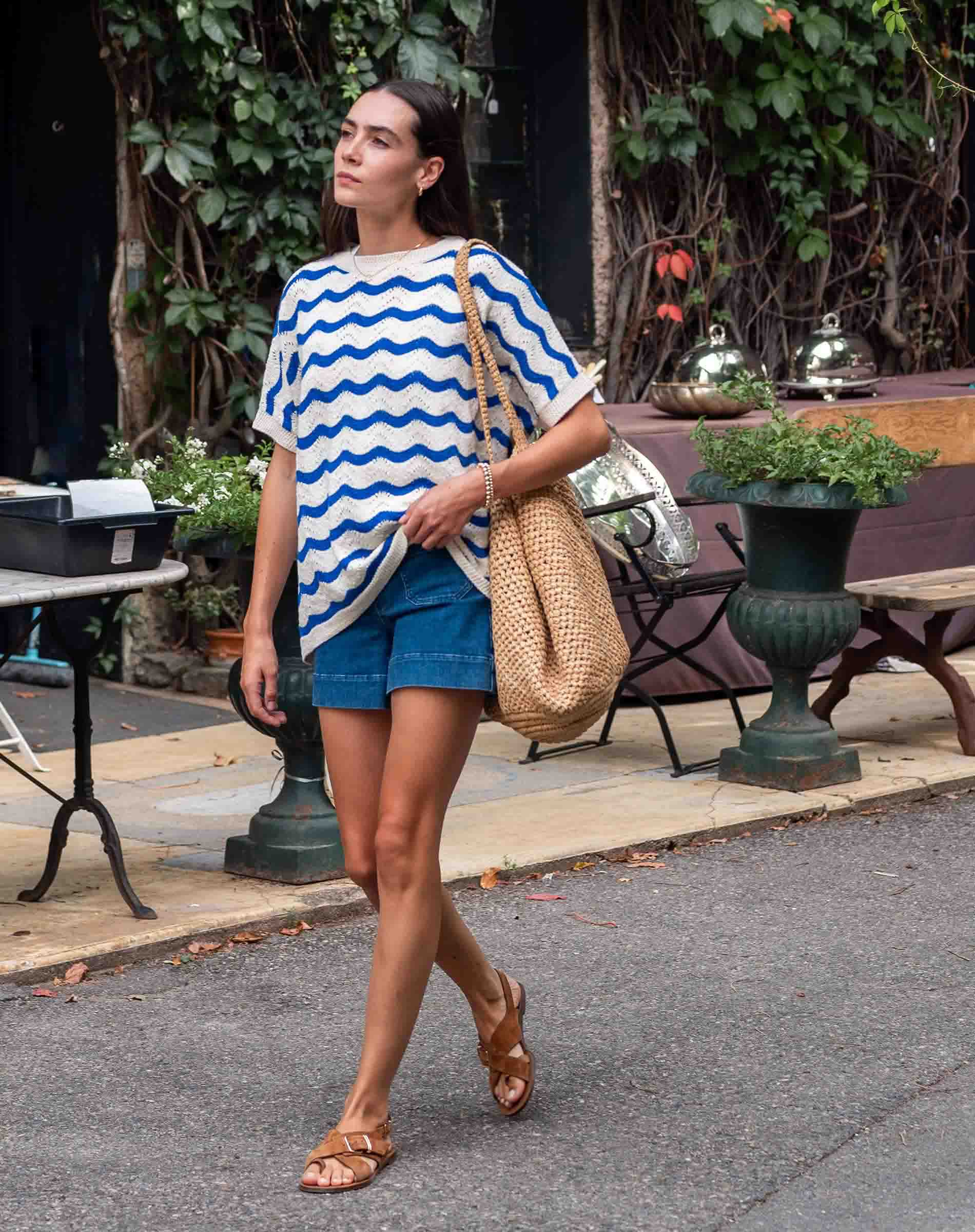 Woman walking outdoors wearing a blue and white striped shirt and denim shorts.