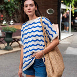 Woman wearing a blue and white striped shirt with denim shorts, holding a woven bag on a street.