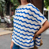 Woman wearing a white and blue wave-patterned top outdoors.