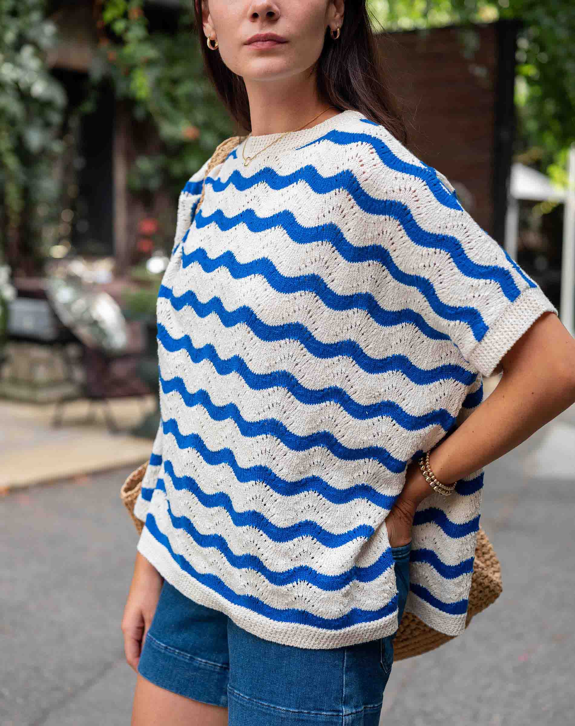 Woman wearing a white and blue wave-patterned top outdoors.