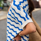 Person wearing a white sweater with blue wave patterns outdoors