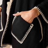 Close-up of the cream and black whipped stitch detail on a knit travel wrap.