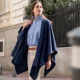 Model in navy whipstitch travel wrap over a blue striped shirt and white pants.