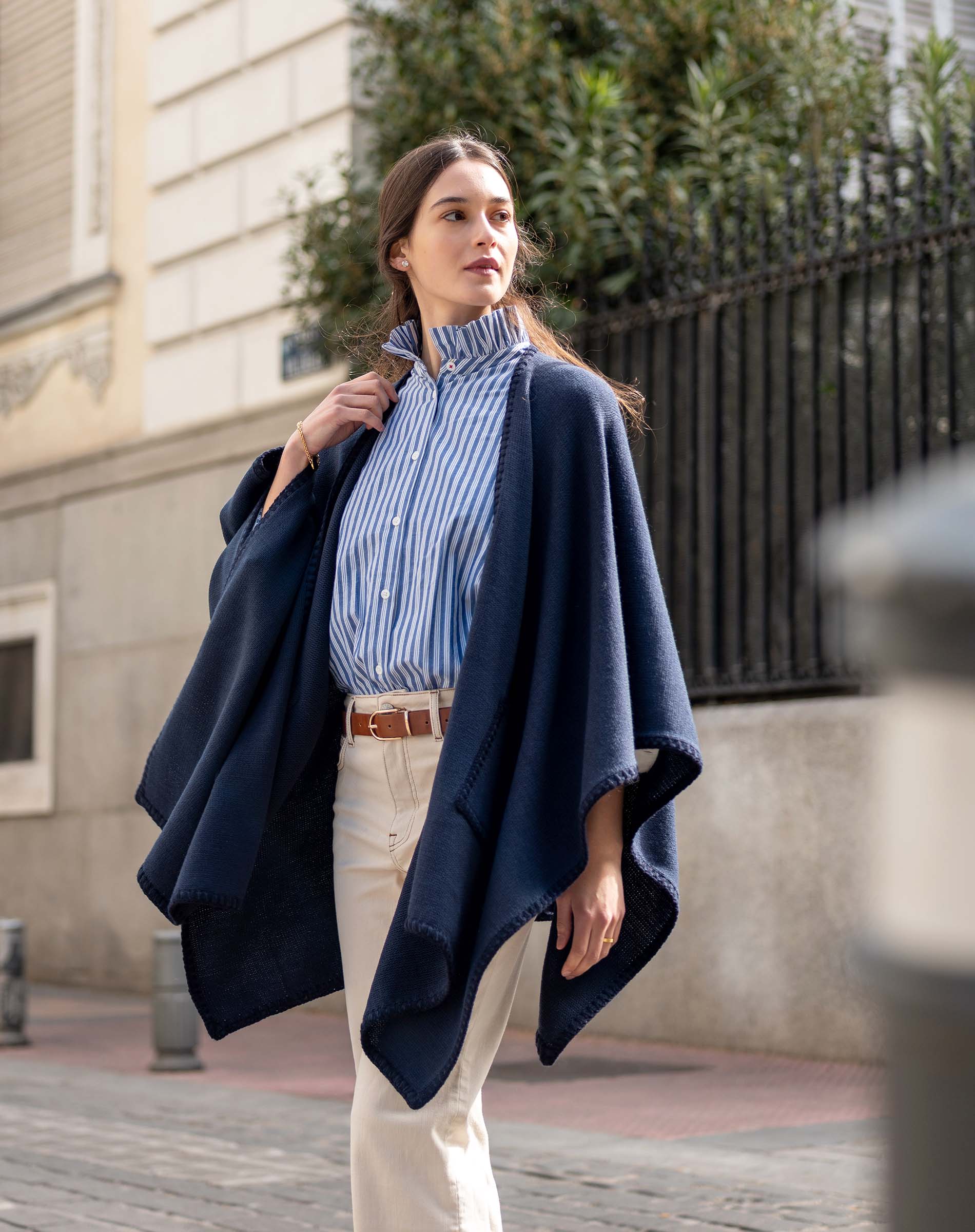 Model in navy whipstitch travel wrap over a blue striped shirt and white pants.