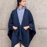 Navy whipstitch travel wrap with oversized pockets over a striped shirt and beige pants.