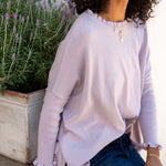 Woman wearing a light pink sweater sitting next to a lavender plant