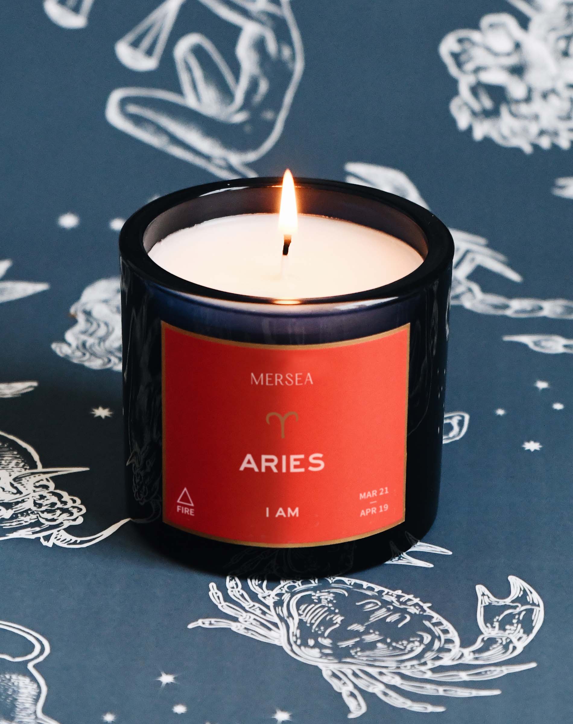 Candle with 'Mersea' label on a dark background with zodiac designs