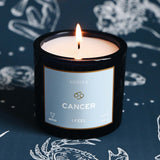 Candle labeled 'Cancer' from the brand 'Mersea' on a dark background with astrological designs.