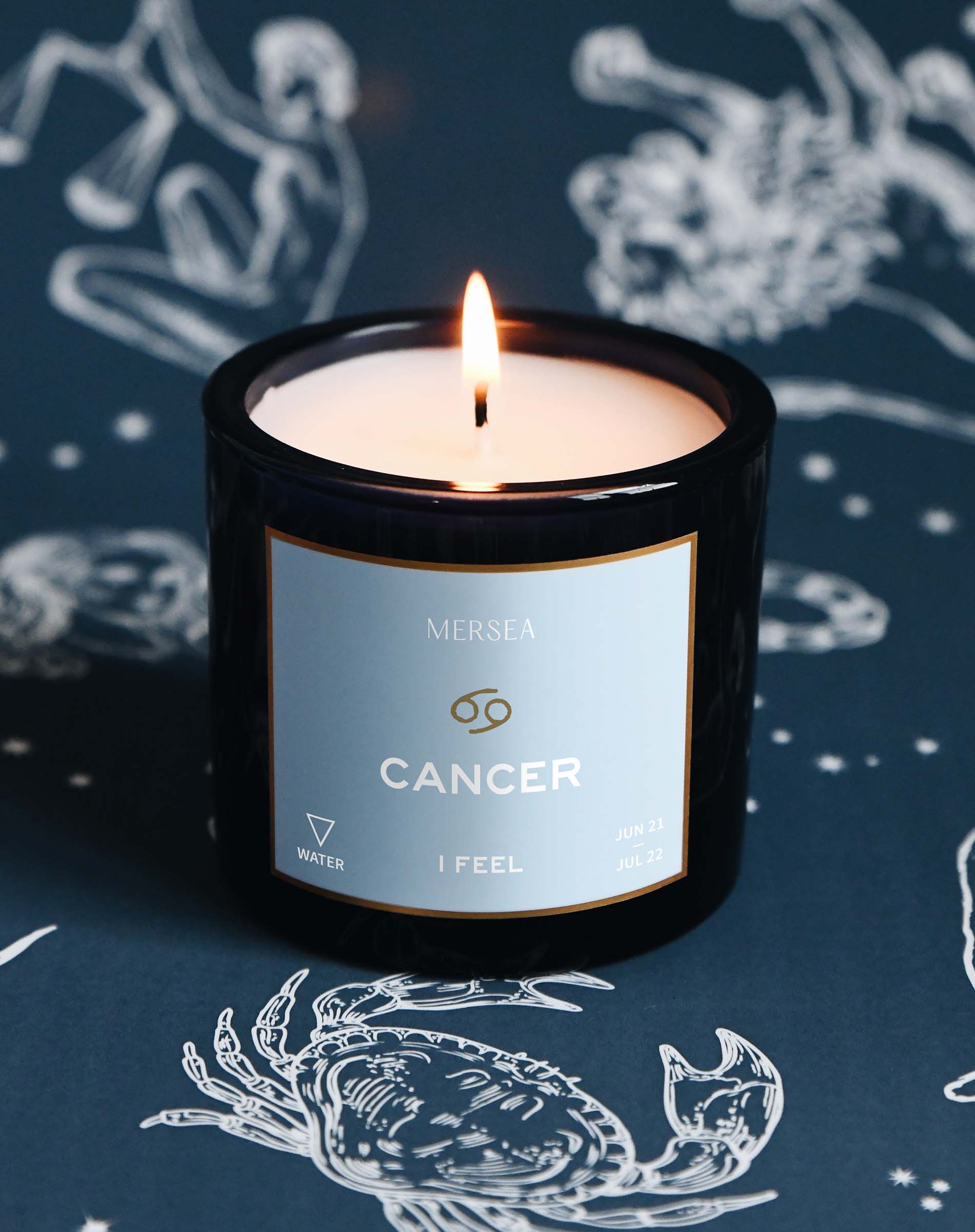 Candle labeled 'Cancer' from the brand 'Mersea' on a dark background with astrological designs.
