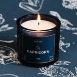 Candle in a black container labeled 'Capricorn' by Mersea on a dark background with astrological designs.