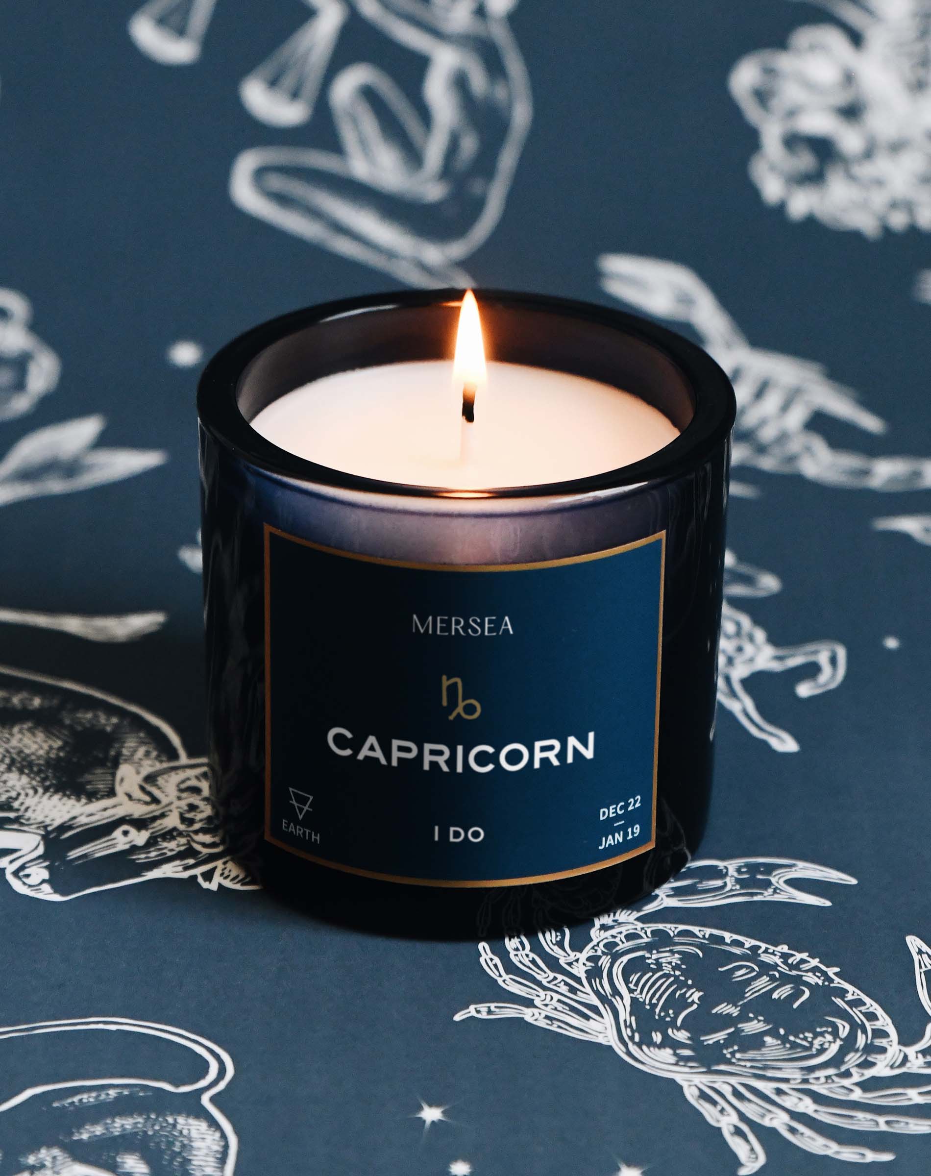 Candle in a black container labeled 'Capricorn' by Mersea on a dark background with astrological designs.