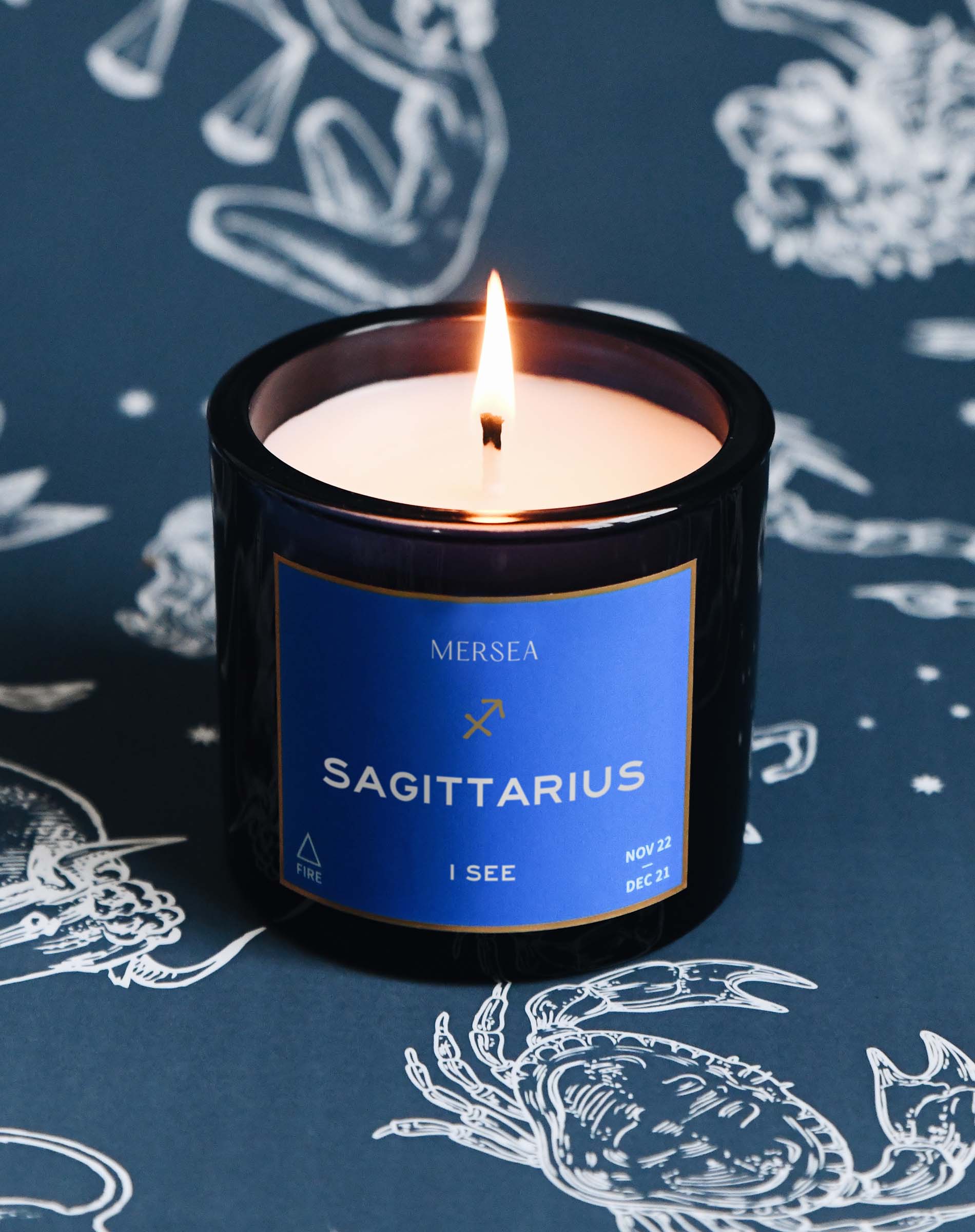 Scented candle labeled 'Sagittarius' by Mersea on a dark background with zodiac designs.