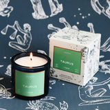 Candle and packaging with 'Taurus' label on a zodiac-themed background