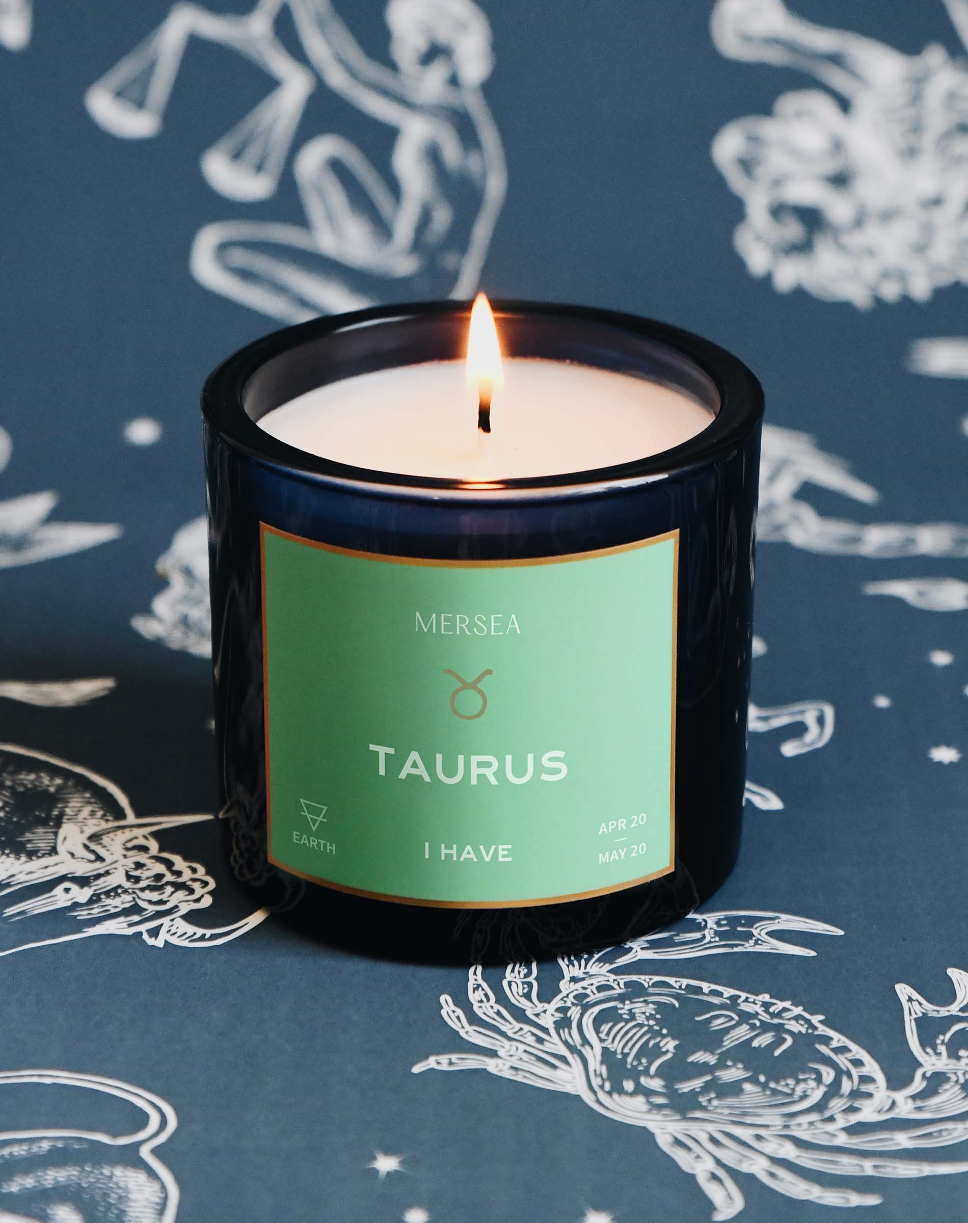 Candle with a 'Mersea' label on a blue background with zodiac designs