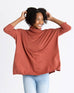 woman wearing mersea newport sweater in sienna color with a split front turtleneck and ribbed sleeves with hands held to sides of head
