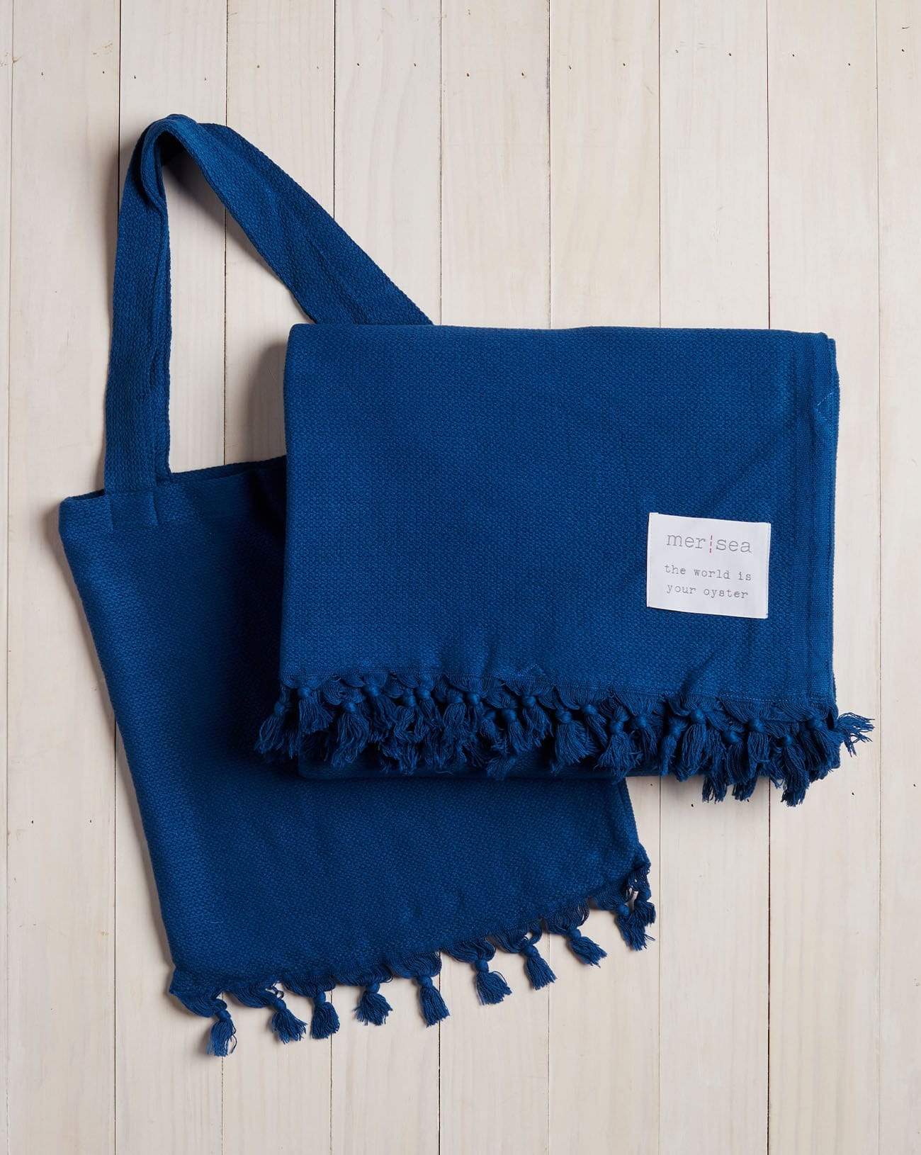 blue beach blanket with fringe and a matching bag on a white wood background