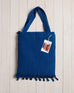 blue beach bag with fringe at the bottom on a white wood background