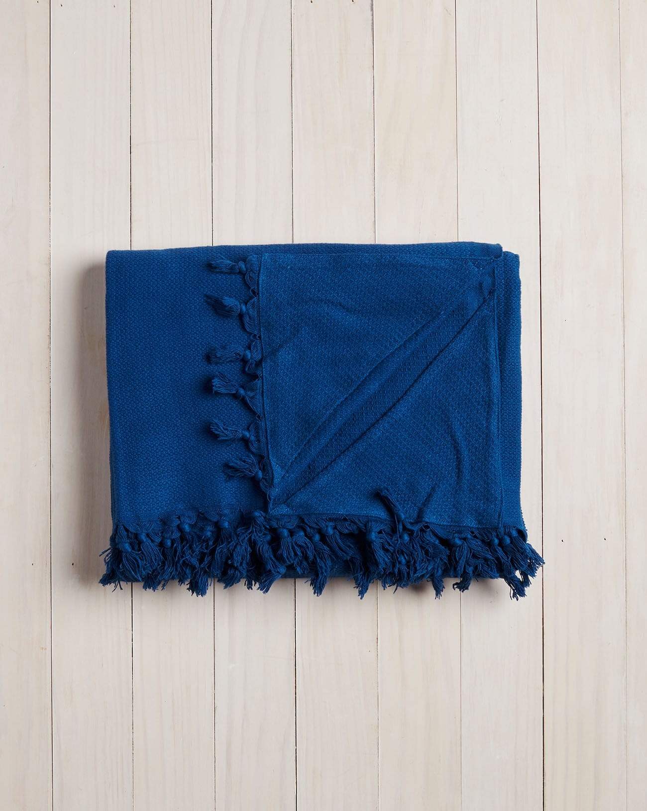 folded blue beach blanket with fringe on a white wood background