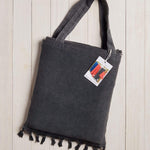 dark grey beach bag with fringe at the bottom on a white wood background