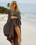 female wrapped in dark grey beach blanket with fringe walking in the san on the beach 