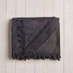 folded dark grey beach blanket with fringe on a white wood background