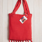 red beach bag with fringe at the bottom on a white wood background