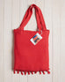 red beach bag with fringe at the bottom on a white wood background