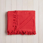 folded red beach blanket with fringe on a white wood background