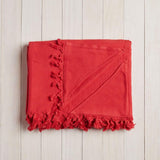 folded red beach blanket with fringe on a white wood background