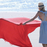 female laying down red blanket with fringe onto in the sand on the beach near the ocean