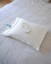 white satin sleep mask and pillowcase set with blue details laying on top of eachother on a bed