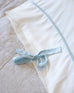 close up of white satin pillow case with light blue tie at one end of the pillow laying on a bed