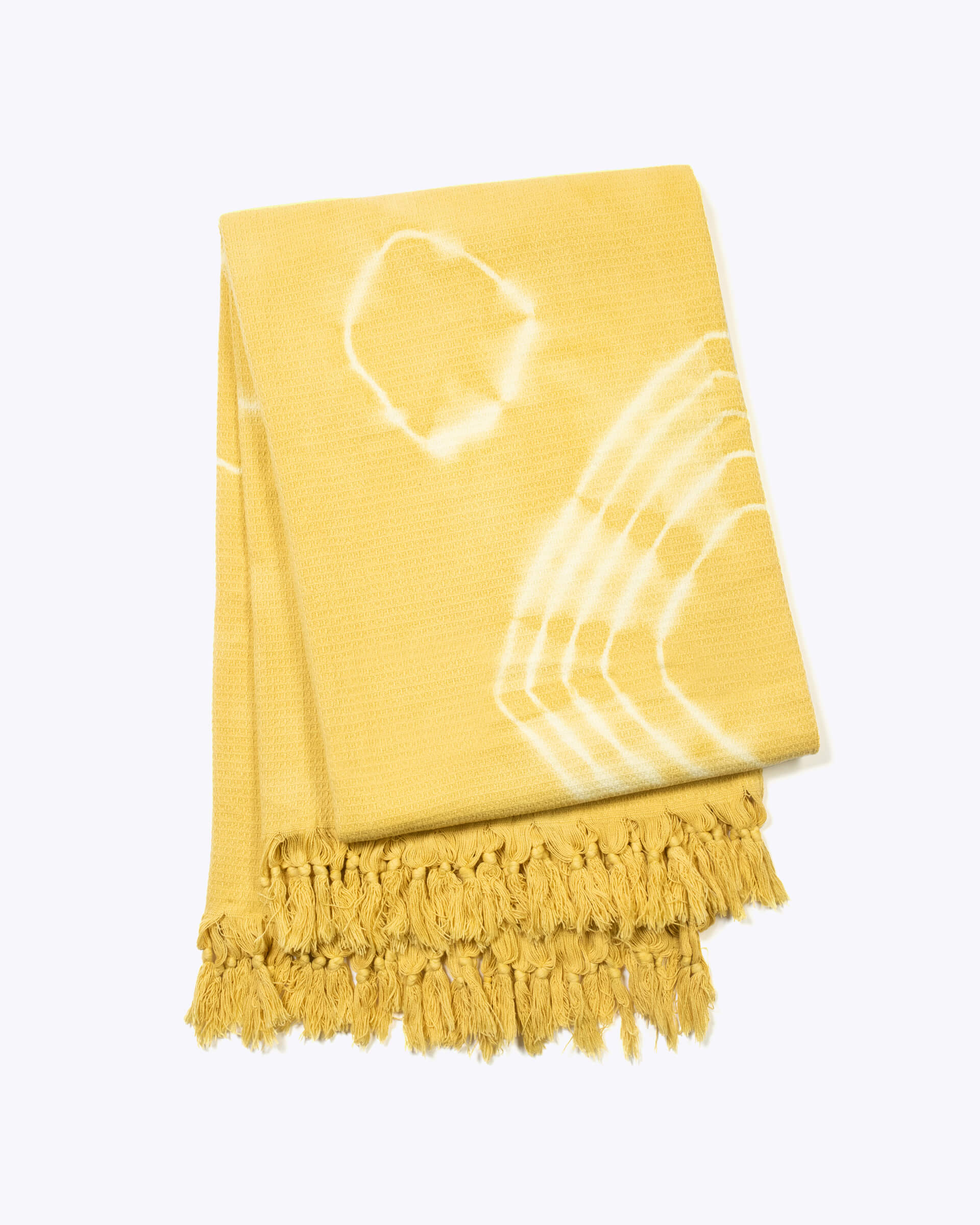 yellow hand-dyed shibori blanket with fringe folded up on a white background