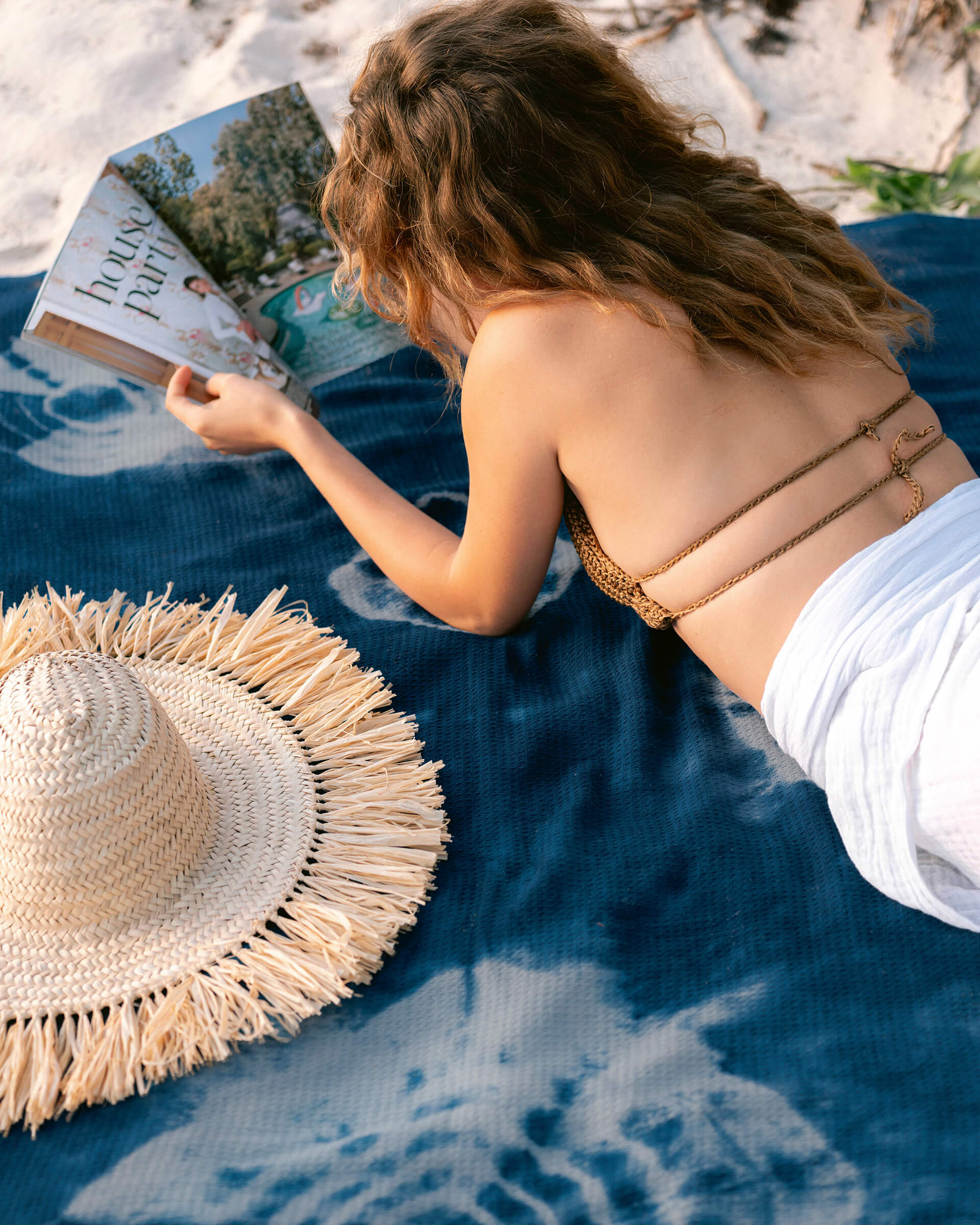 Summer House Blanket in Indigo Shiboriafemale laying on blue shibori blanket reading a magazine with a straw hat next to her on the beach